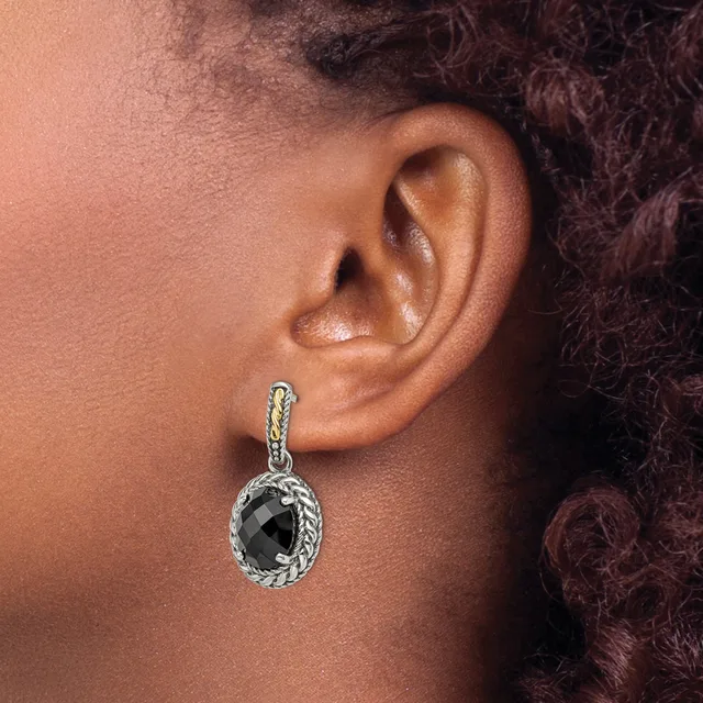 A close-up of a person's ear wearing a silver dangle earring with a twisted rope design and a faceted black stone pendant.