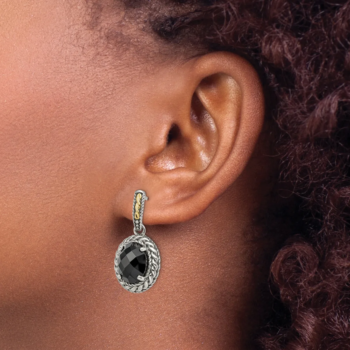 A close-up of a person's ear wearing a silver dangle earring with a twisted rope design and a faceted black stone pendant.