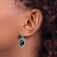 A close-up of a person's ear wearing a silver dangle earring with a twisted rope design and a faceted black stone pendant.