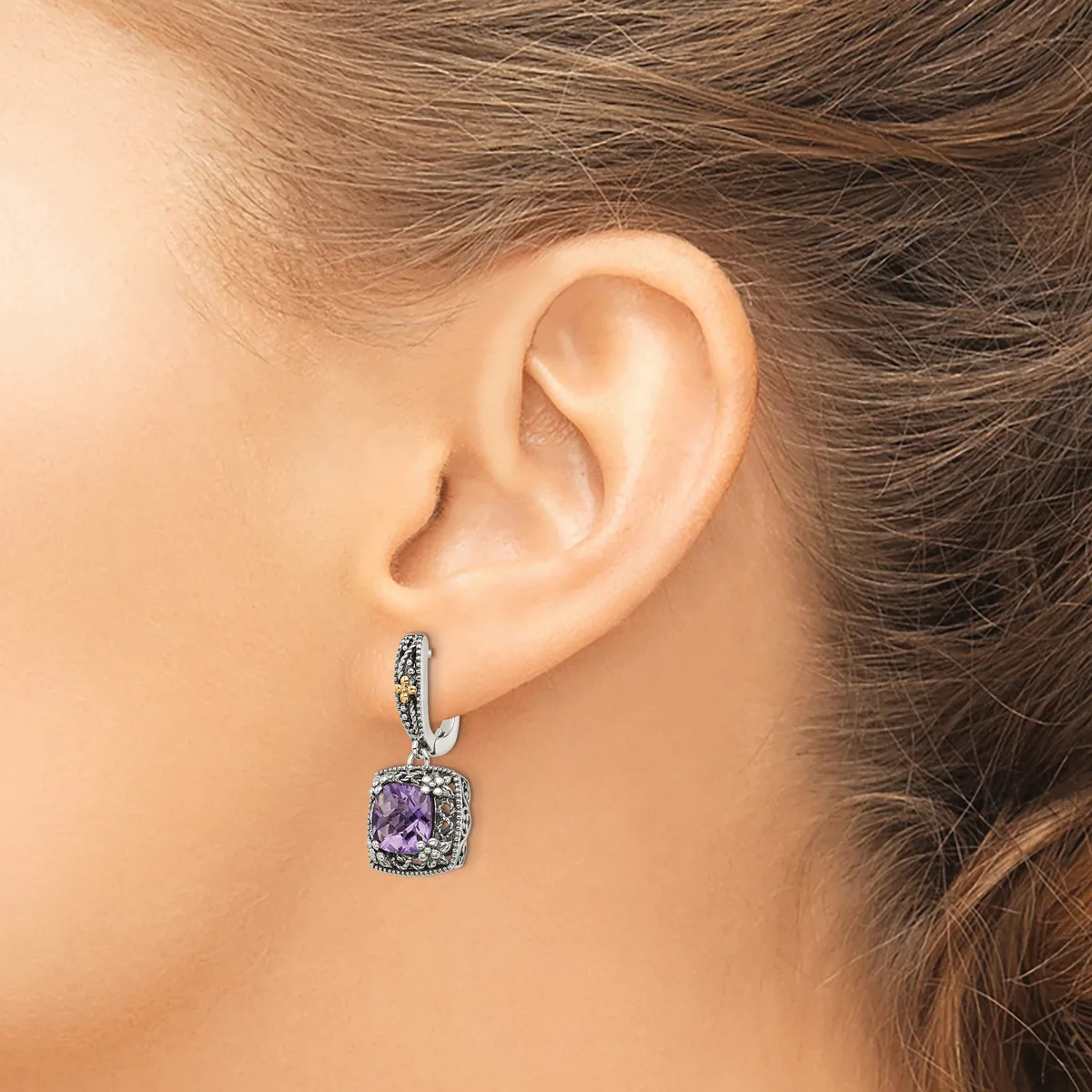 A woman wearing a silver hoop earring with a dangling cushion-cut amethyst pendant surrounded by small diamonds.