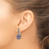 A woman wearing a silver hoop earring with a dangling cushion-cut amethyst pendant surrounded by small diamonds.
