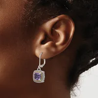 A person wearing a silver drop earring with a cushion-cut purple gemstone surrounded by a halo of small diamonds on a hinged hook post.