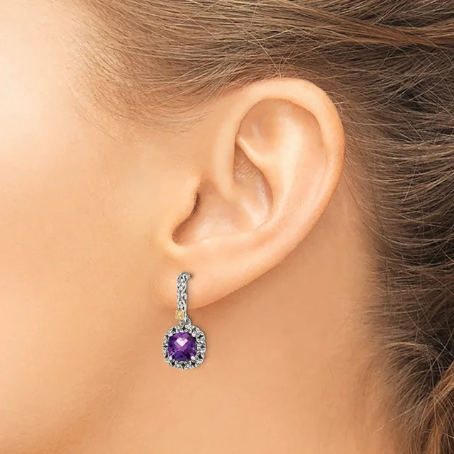 A woman wears a dangling earring with a round purple gemstone surrounded by small diamonds set in white metal, shown on her ear from a side profile view.