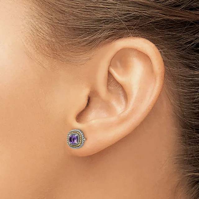 A person wearing a small round stud earring with a purple gemstone center surrounded by a halo of small diamonds, shown on an earlobe.