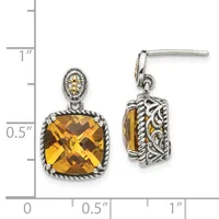 A pair of silver drop earrings with cushion-cut golden citrine stones surrounded by ornate scrollwork, shown with a measurement scale.