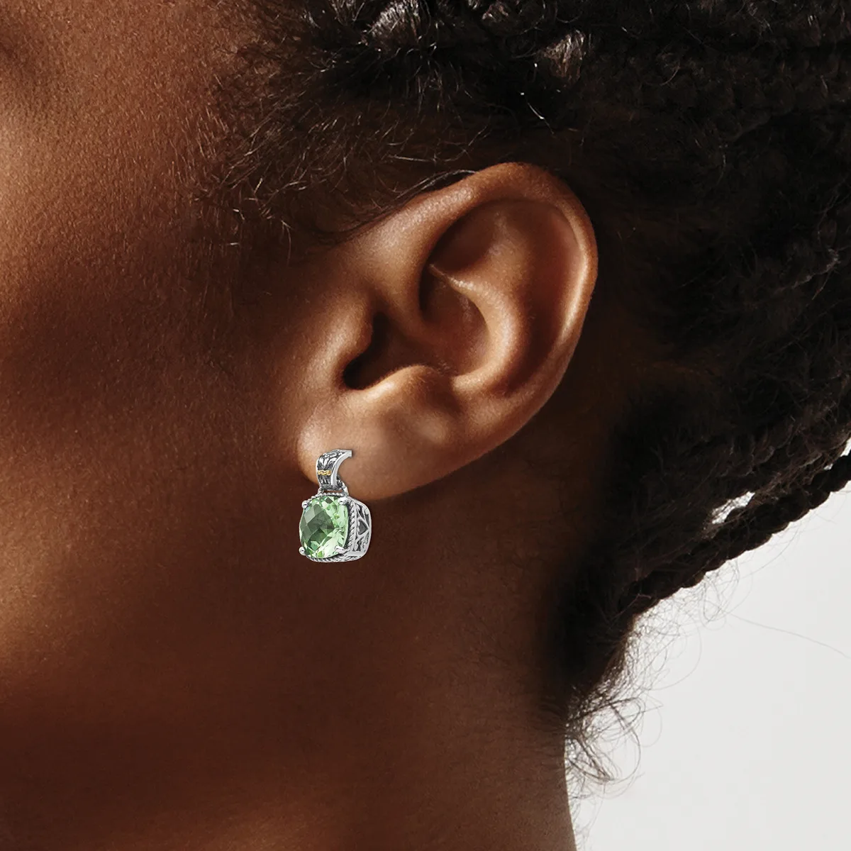 A person wearing a silver earring with a green square stone surrounded by small diamonds, shown from the side profile against a neutral background.