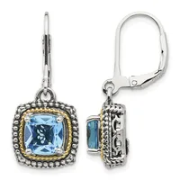 Pair of silver dangle earrings with cushion-cut blue topaz centers surrounded by beaded silver frames with gold-tone accents and leverback closures, shown from front and side views.