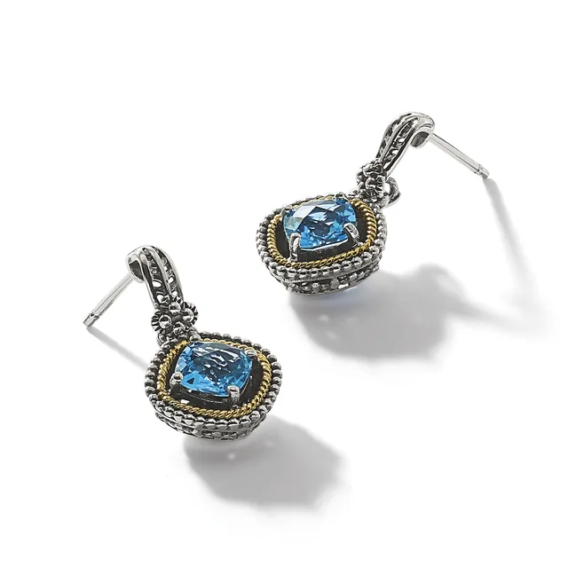 Pair of silver and gold-toned drop earrings with cushion-cut blue topaz stones set in ornate frames with beaded borders and decorative posts.