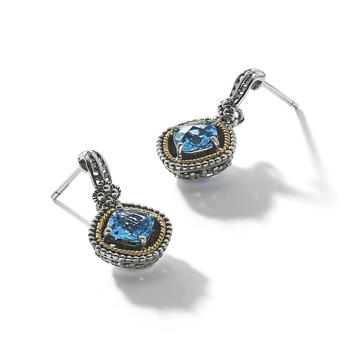 Pair of silver and gold-toned drop earrings with cushion-cut blue topaz stones set in ornate frames with beaded borders and decorative posts.