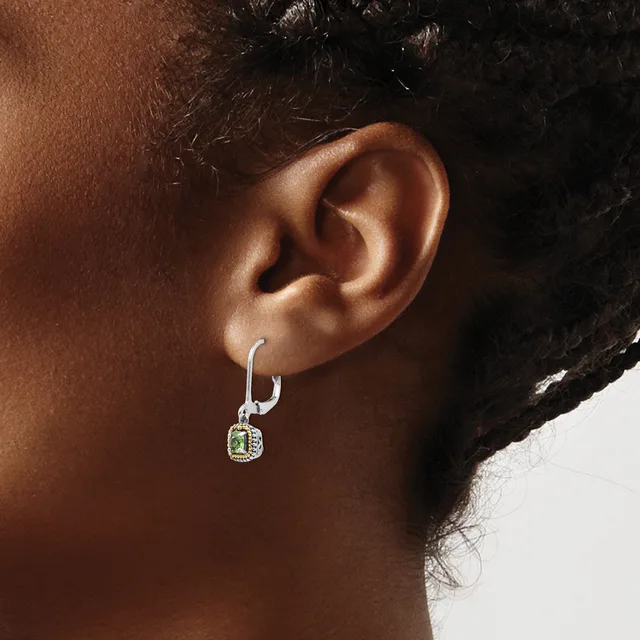 A person wearing a silver hoop earring with a small square pendant featuring a green stone and diamond accents.