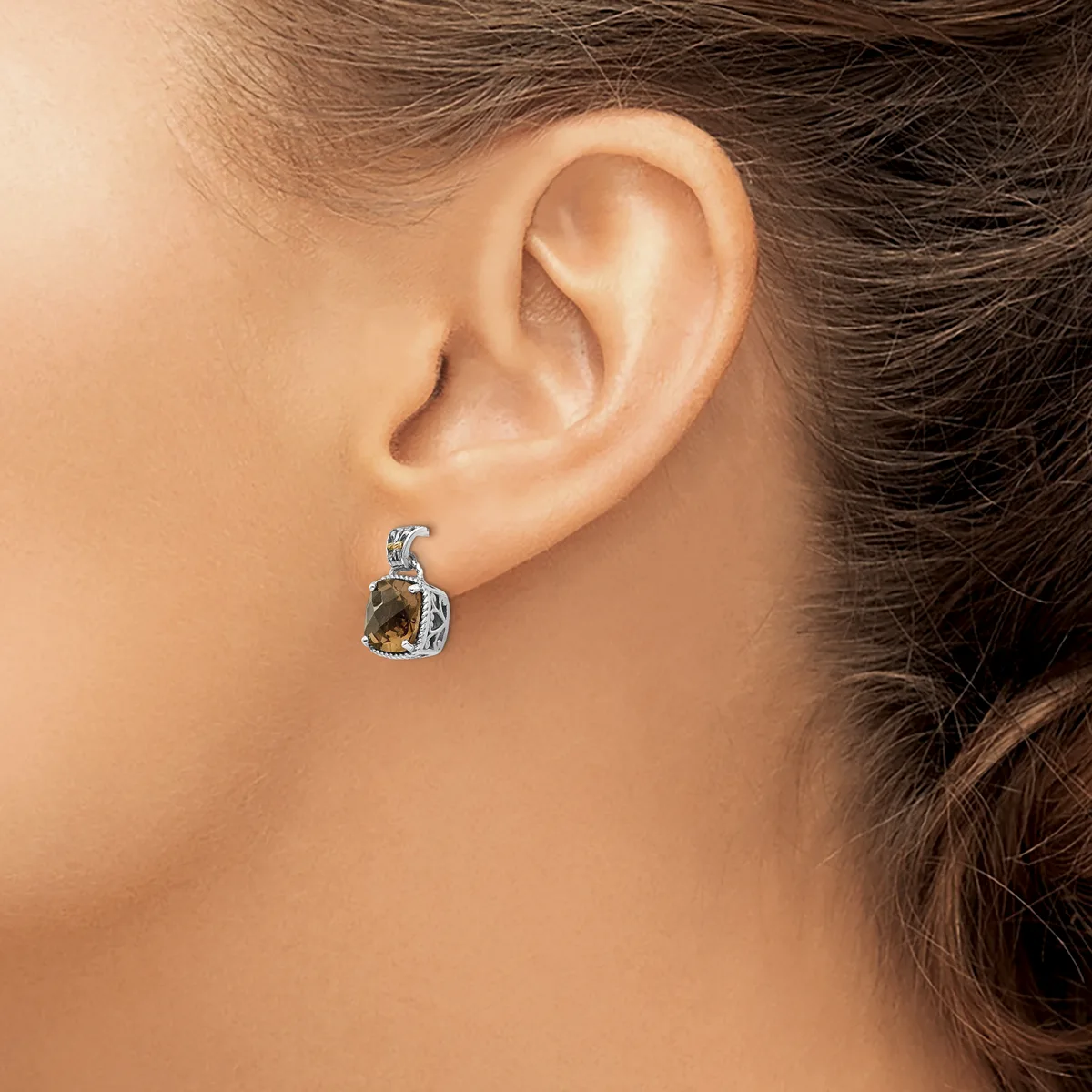 A woman wearing a small silver earring with a golden-brown faceted stone and decorative metalwork, shown from the side view of her ear and neck.