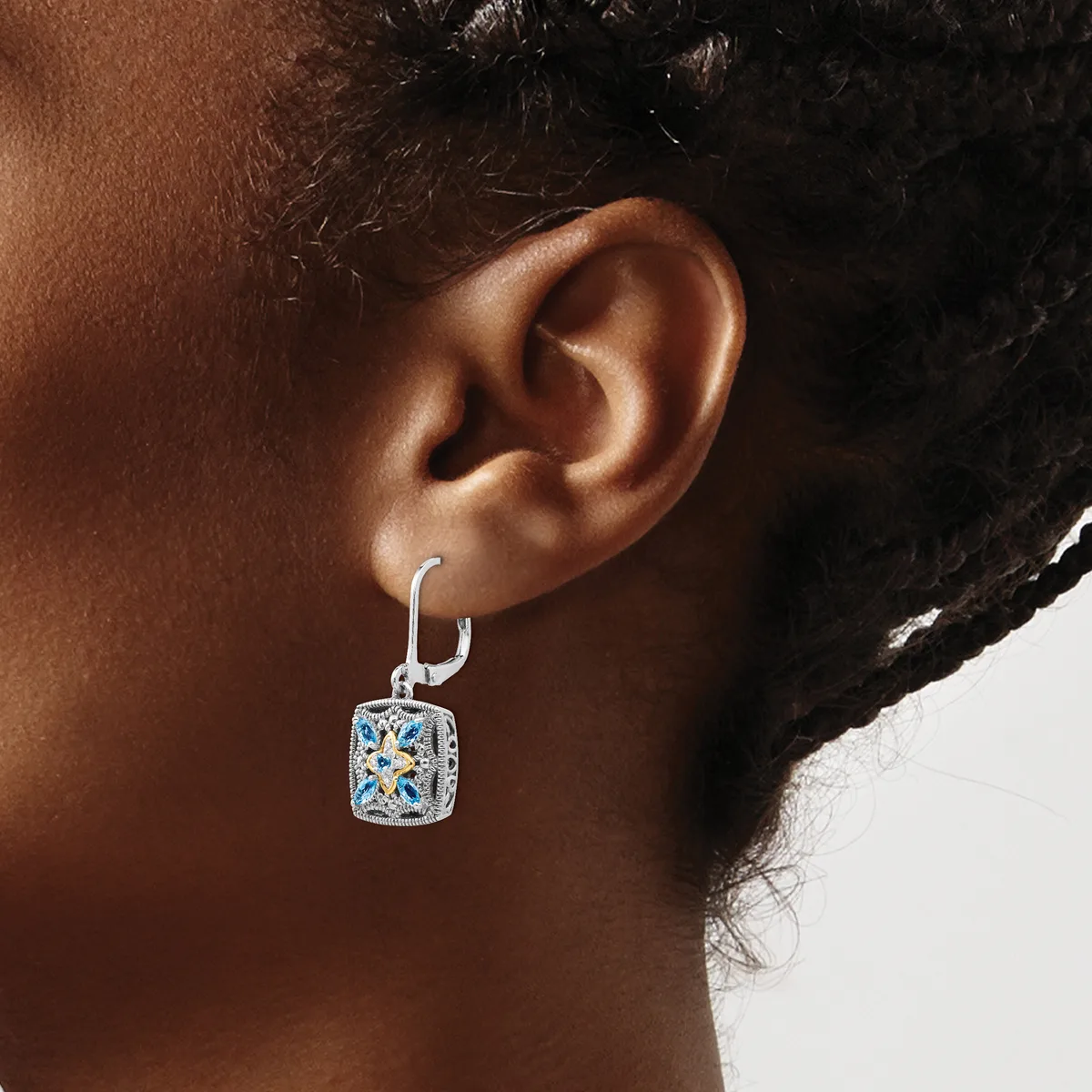 A person wearing a silver drop earring with a square pendant featuring blue stone inlay in a geometric pattern, shown from the side view of their ear.