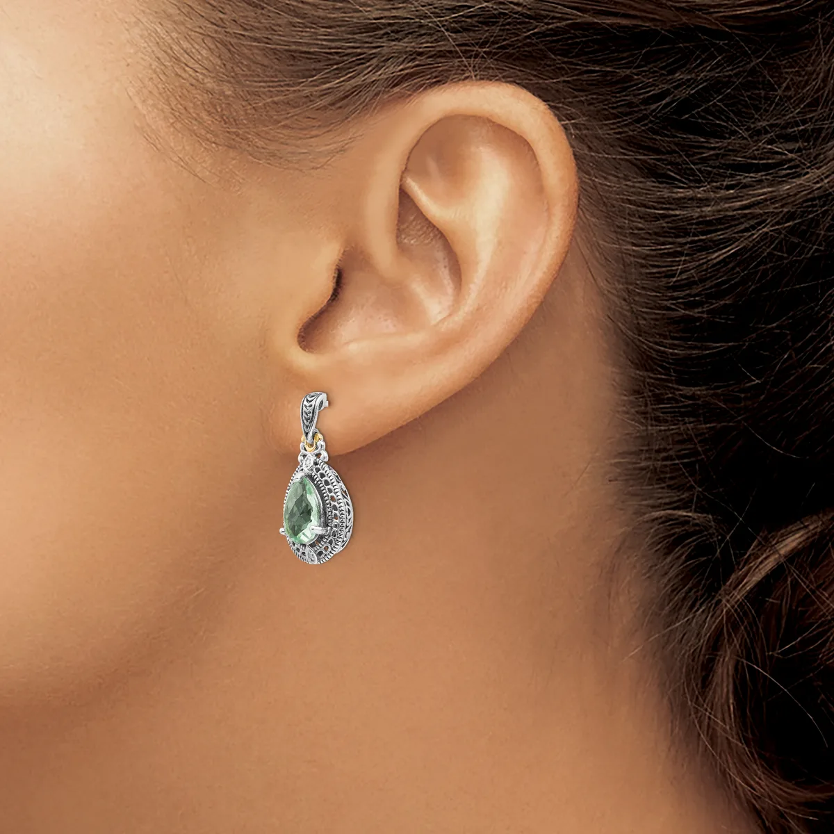 A woman wearing a teardrop-shaped earring with a pale green stone surrounded by small diamonds in a white metal setting.