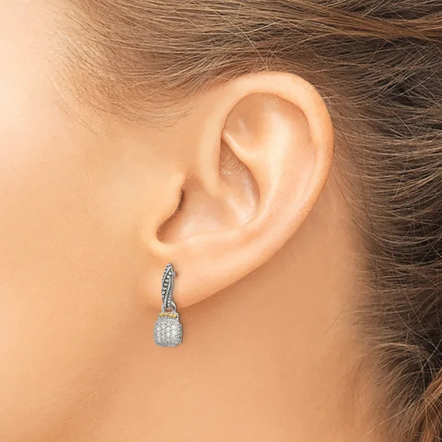 A person wearing a dangling silver earring with a twisted band and a pear-shaped cluster of small stones, shown from the side against their ear.