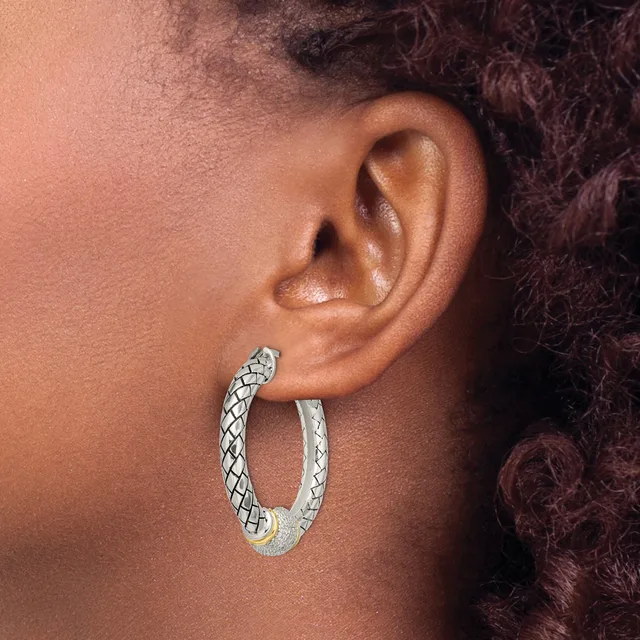 A person wearing textured silver hoop earrings with a crosshatch pattern, shown from the side profile against their ear.