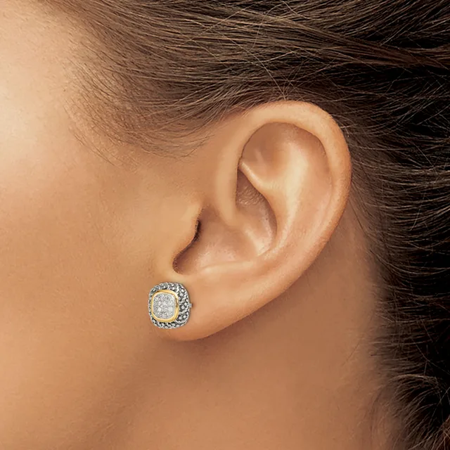 A close-up view of a person's ear wearing a round stud earring with a center diamond surrounded by a halo of smaller stones in white metal.