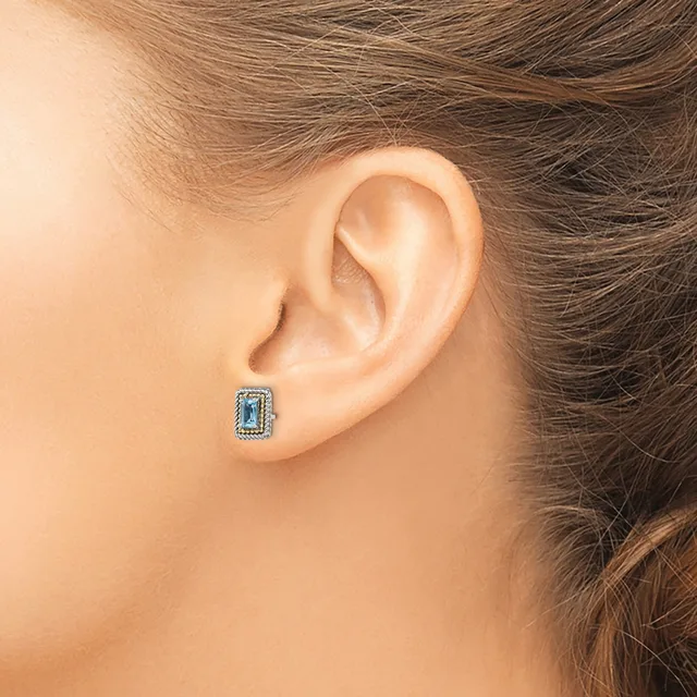 A person wearing a small rectangular stud earring with a blue stone surrounded by a decorative border, shown from the side view of their ear.
