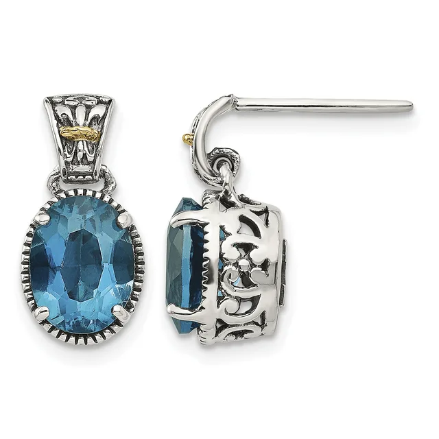 A pair of silver drop earrings with ornate scrollwork caps featuring blue oval faceted gemstones set in decorative bezels.
