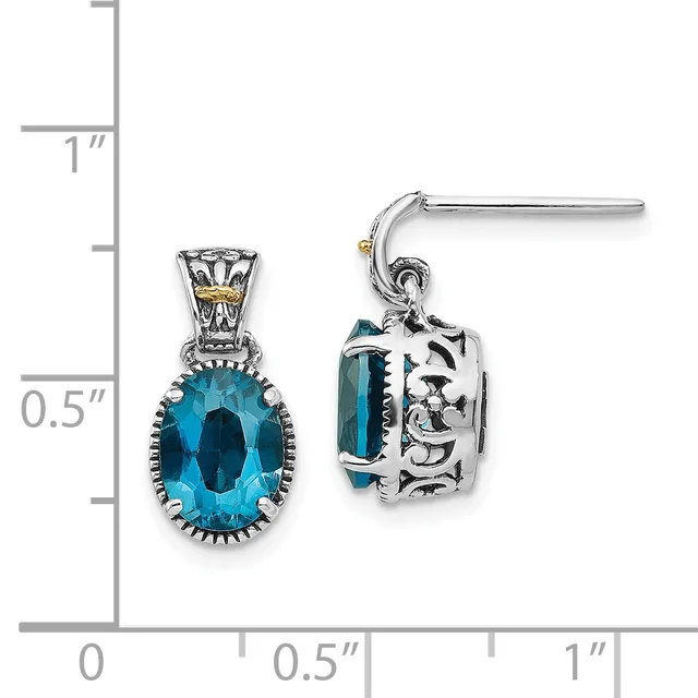 A pair of silver dangle earrings featuring oval-cut blue topaz stones set in ornate scrollwork settings, displayed against a measurement scale.