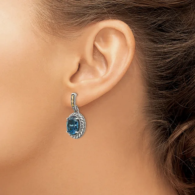 A woman wearing a teardrop-shaped earring with a blue stone surrounded by a textured silver setting and matching silver ear wire.