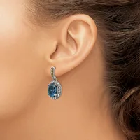 A woman wearing a teardrop-shaped earring with a blue stone surrounded by a textured silver setting and matching silver ear wire.