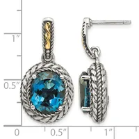 Pair of silver dangle earrings with twisted rope borders surrounding round faceted blue topaz stones, with gold-toned accents on the posts, shown against a measurement scale.