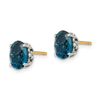 A pair of oval-cut deep blue topaz stud earrings set in two-tone metal with decorative silver-colored bezels and gold posts.