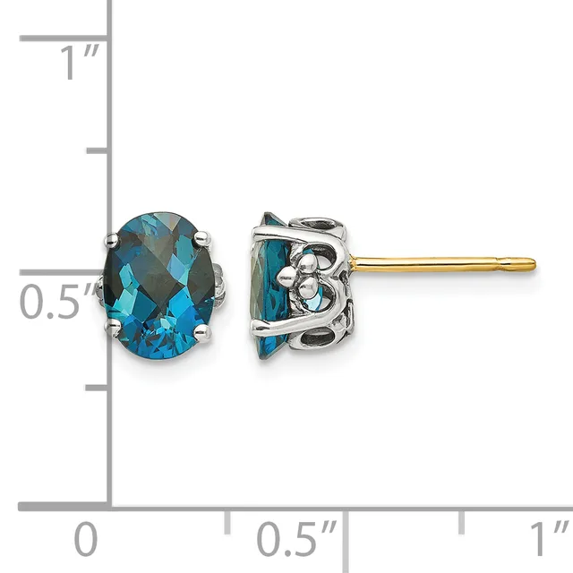 A pair of blue topaz oval stud earrings with decorative silver settings and gold posts, shown next to a ruler measuring approximately half an inch in height.