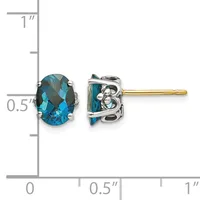 A pair of blue topaz oval stud earrings with decorative silver settings and gold posts, shown next to a ruler measuring approximately half an inch in height.