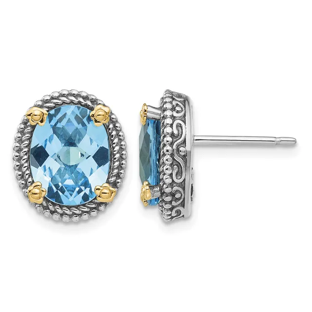 Pair of oval stud earrings featuring faceted blue topaz stones set in ornate silver frames with gold-tone accents, shown from front and side views.