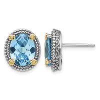 Pair of oval stud earrings featuring faceted blue topaz stones set in ornate silver frames with gold-tone accents, shown from front and side views.