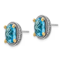 Pair of oval stud earrings featuring blue topaz stones set in silver with gold-tone accents and beaded borders, shown from the front.