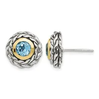 Pair of round stud earrings featuring blue topaz stones set in gold bezels, surrounded by twisted silver bezels with braided detailing, shown from front and side views.