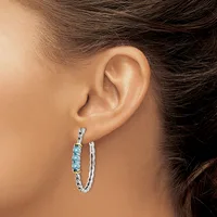 A woman wearing a pair of silver hoop earrings with blue gemstone accents on one side, shown from the side profile against her ear.