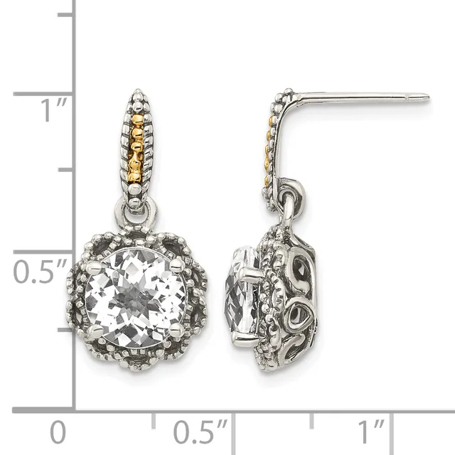 A pair of two-tone dangle earrings with cushion-cut clear stones surrounded by ornate metalwork and textured posts, shown against a measurement scale.