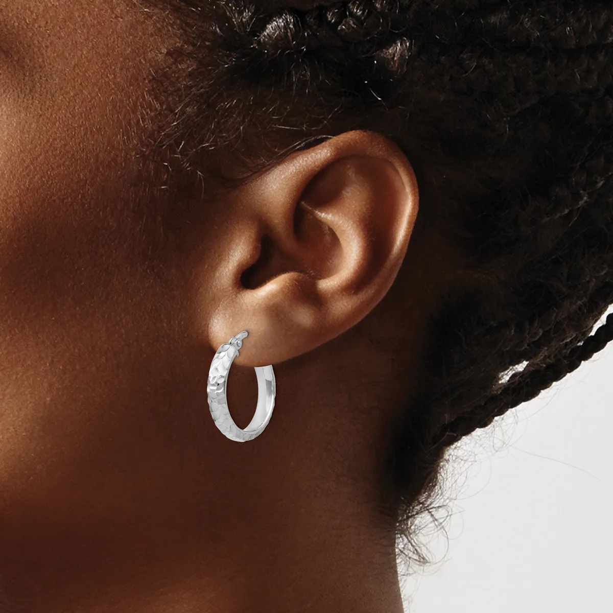 A person wearing a textured silver hoop earring in their earlobe, shown in profile against a neutral background.