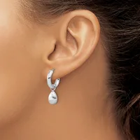 A woman wearing silver hoop earrings with teardrop-shaped pendant charms hanging from her earlobes.