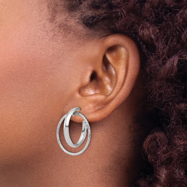 A person wearing a pair of double oval hoop earrings with a textured finish in silver-tone metal, shown from the side view against their ear.