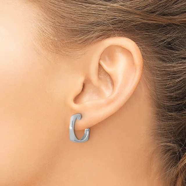 A person wearing a small curved C-shaped hoop earring in brushed silver-toned metal in their earlobe.
