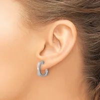 A person wearing a small curved C-shaped hoop earring in brushed silver-toned metal in their earlobe.