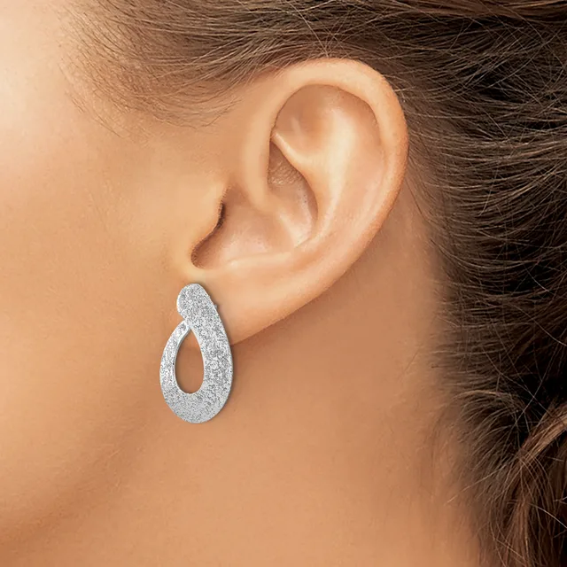 A woman wearing a textured silver teardrop-shaped hoop earring with an open center, shown from the side view of her ear.