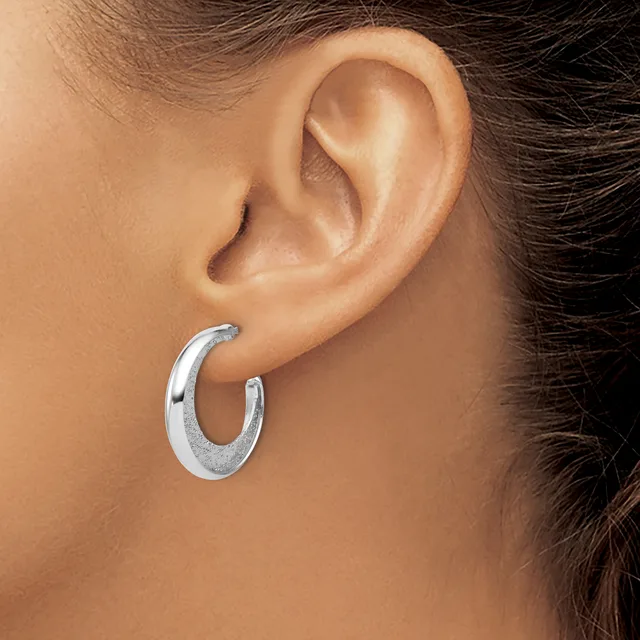 A person wearing a curved silver hoop earring in their earlobe, shown in profile against their neck and shoulder.