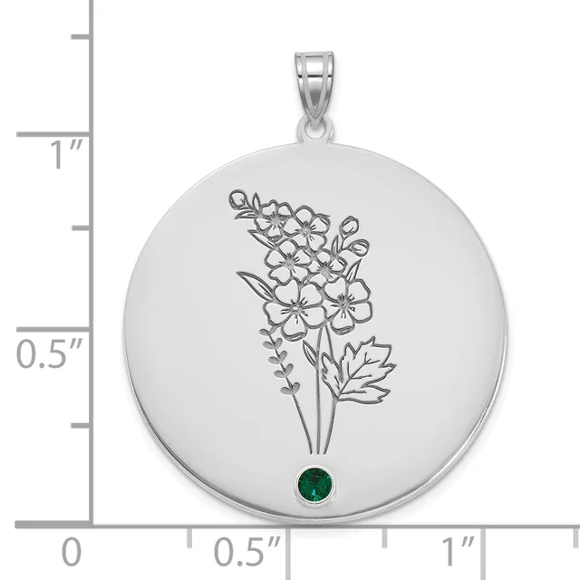 Silver circular pendant with engraved floral bouquet design and a small round green gemstone at the bottom, shown next to a ruler measuring approximately one inch in diameter.