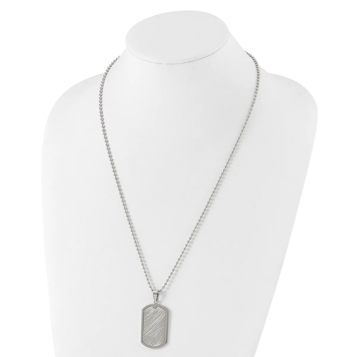 A silver-toned rectangular dog tag pendant with diagonal line texture hangs from a matching ball chain necklace, displayed on a white bust form.