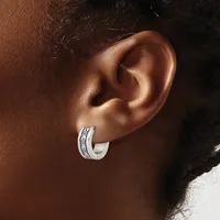 A silver hoop earring with an engraved decorative band worn on the earlobe of a person with brown skin.