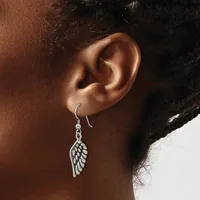A silver wing-shaped dangle earring hangs from a curved hook on a person's earlobe.