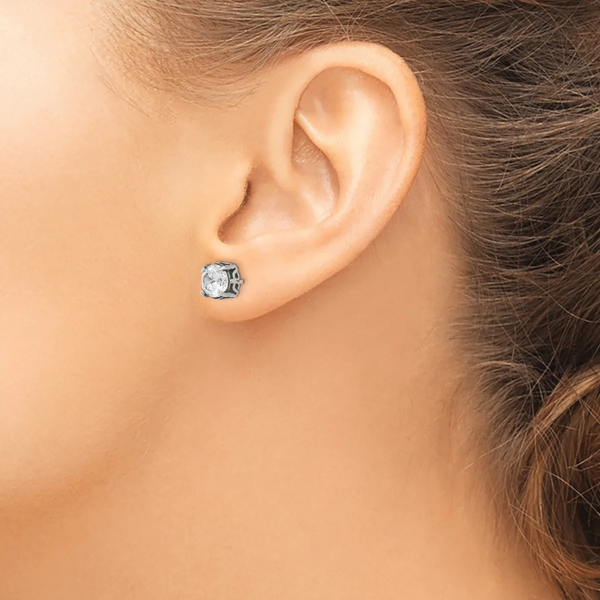 A woman wearing a small square stud earring with a clear faceted stone in a silver-toned setting, shown from the side view near her ear.
