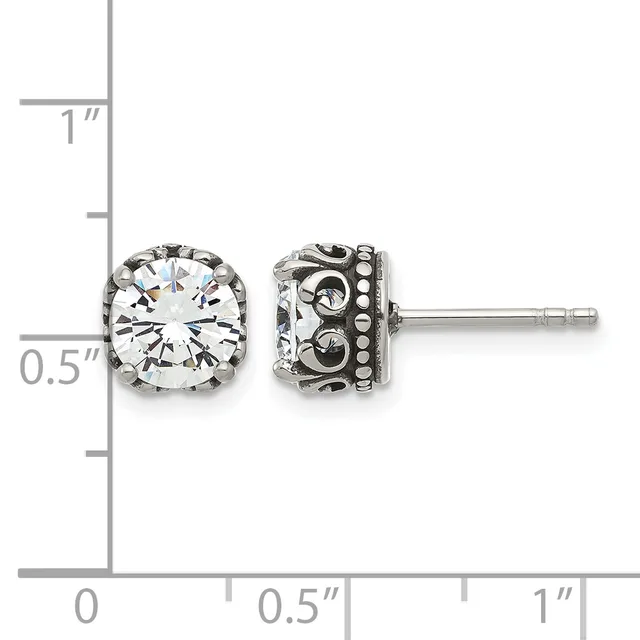 A pair of silver stud earrings with round clear gemstones in ornate filigree settings, shown against a measurement scale.