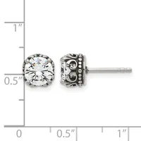 A pair of silver stud earrings with round clear gemstones in ornate filigree settings, shown against a measurement scale.