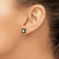 A square stud earring with a clear center stone surrounded by dark metalwork sits on the earlobe of a person shown in profile.